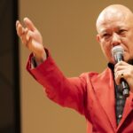 マイクを握り、客席へ手を伸ばして語る鴨頭嘉人