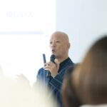 教室で受講生の前に立ち、マイクを持って話す鴨頭嘉人