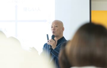 教室で受講生の前に立ち、マイクを持って話す鴨頭嘉人