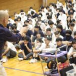 学校の体育館で生徒に向けて話す鴨頭嘉人