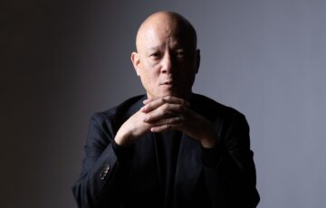 暗い背景で両手を組み、静かに考える鴨頭嘉人