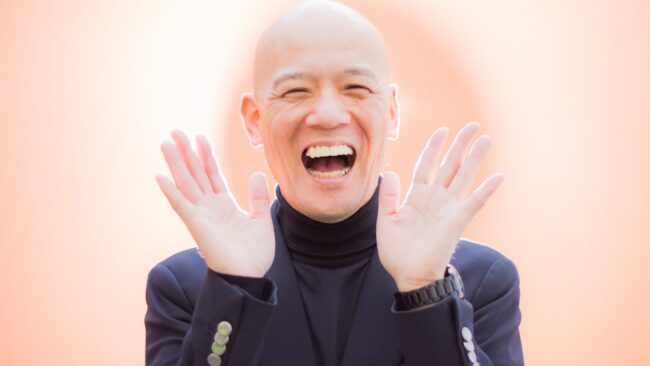 両手を開き、明るい笑顔を見せる鴨頭嘉人
