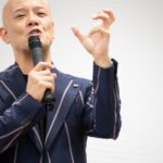 マイクを持ち、指先を使って丁寧に説明する鴨頭嘉人