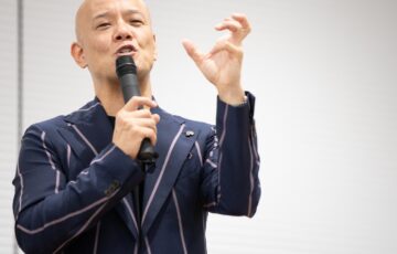 マイクを持ち、指先を使って丁寧に説明する鴨頭嘉人