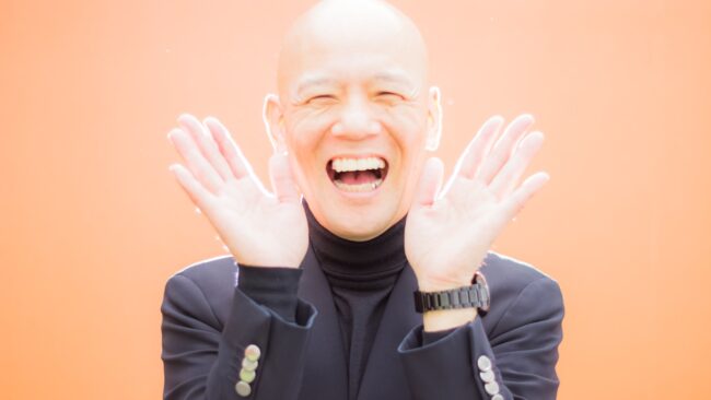 両手を開いて明るい笑顔を見せる鴨頭嘉人